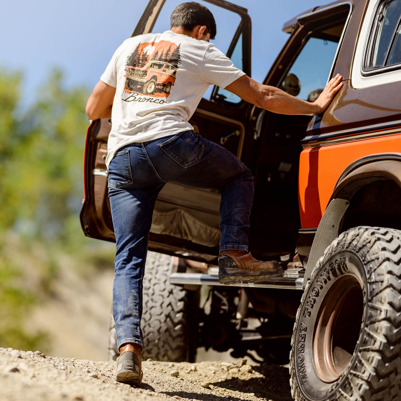 Man getting into an orange truck on a dirt road