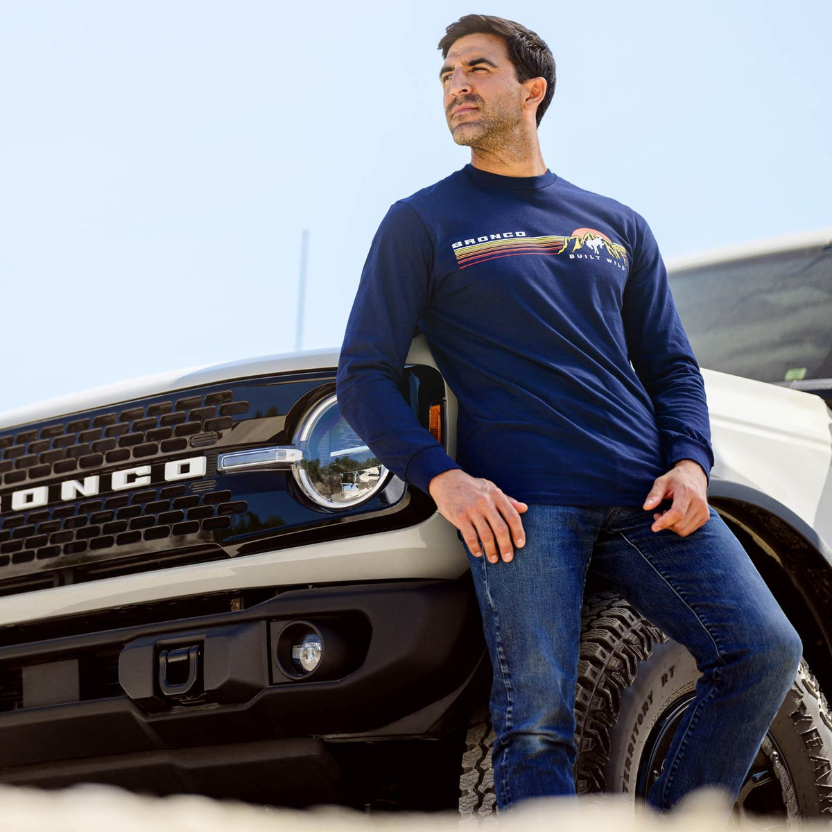 Man wearing a blue long-sleeve shirt with a logo, leaning against a truck.