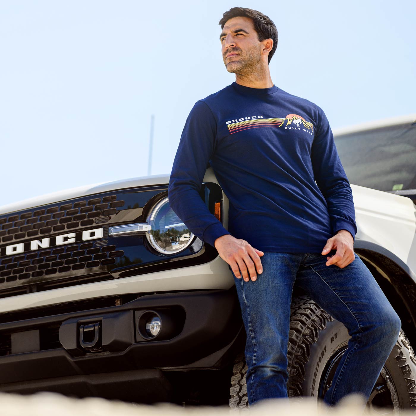 Man wearing a blue long-sleeve shirt with a logo, leaning against a truck.