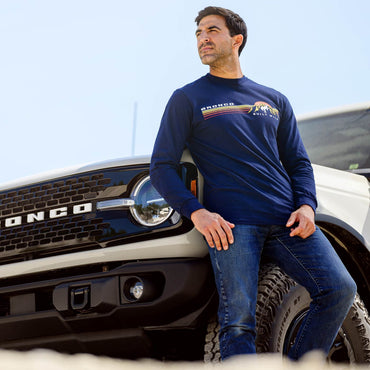 Man wearing a blue long-sleeve shirt with a logo, leaning against a truck.