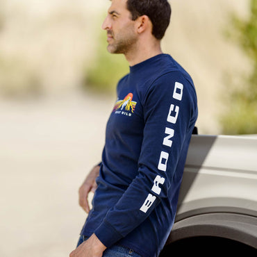 Man wearing a blue long-sleeve shirt with 'Bronco' branding, standing next to a vehicle.