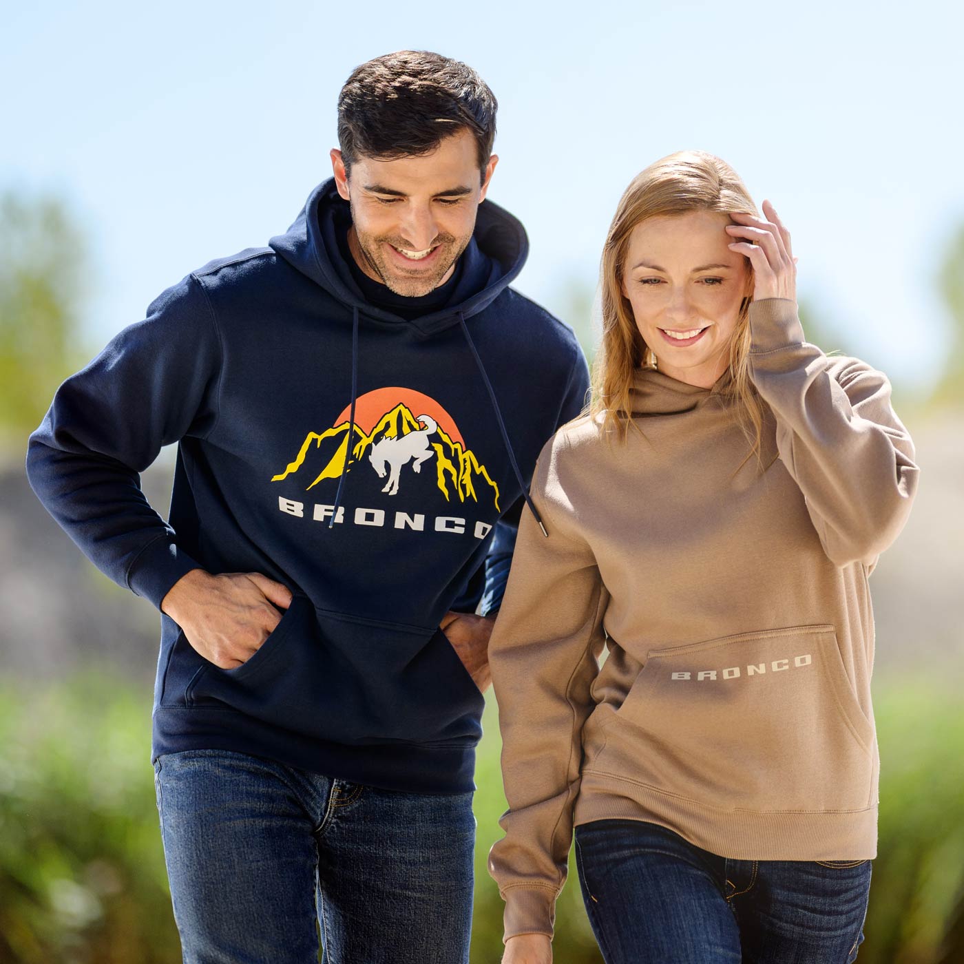 Two people wearing navy and beige Bronco hoodies outdoors.