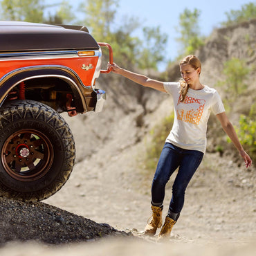 Woman standing next to a red truck on a rocky trail