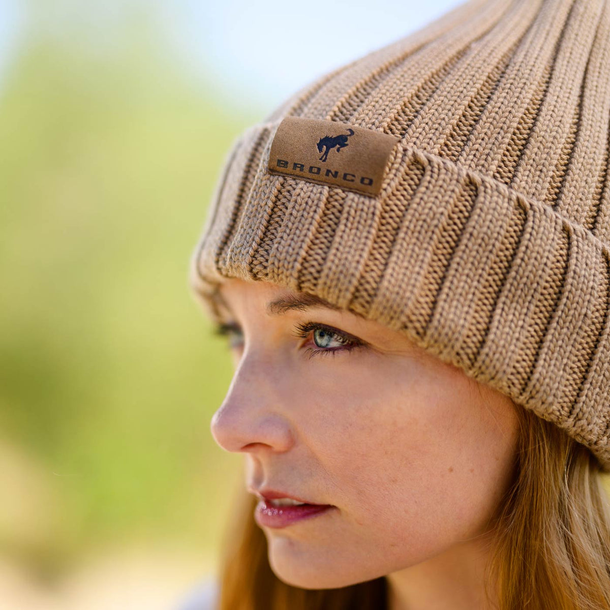 close up of women's face in a knit beige hat with a bronco tag