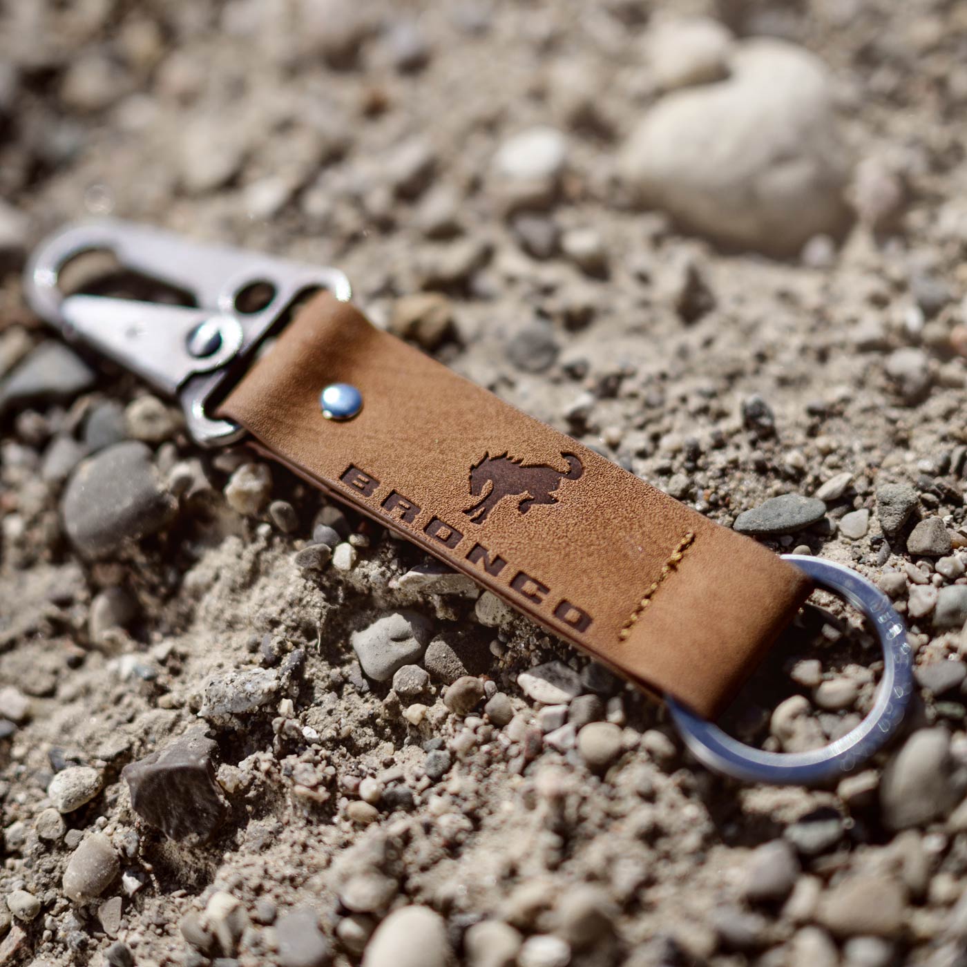 Brown leather keychain with metal clip on a gravel surface