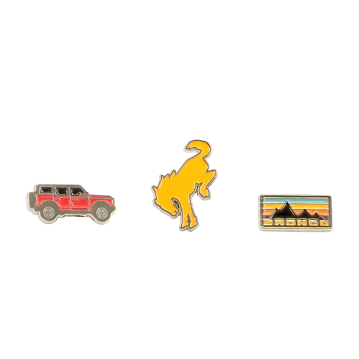 Three enamel pins on a white background: a red car, a yellow dinosaur, and a rectangular badge with mountains and text.