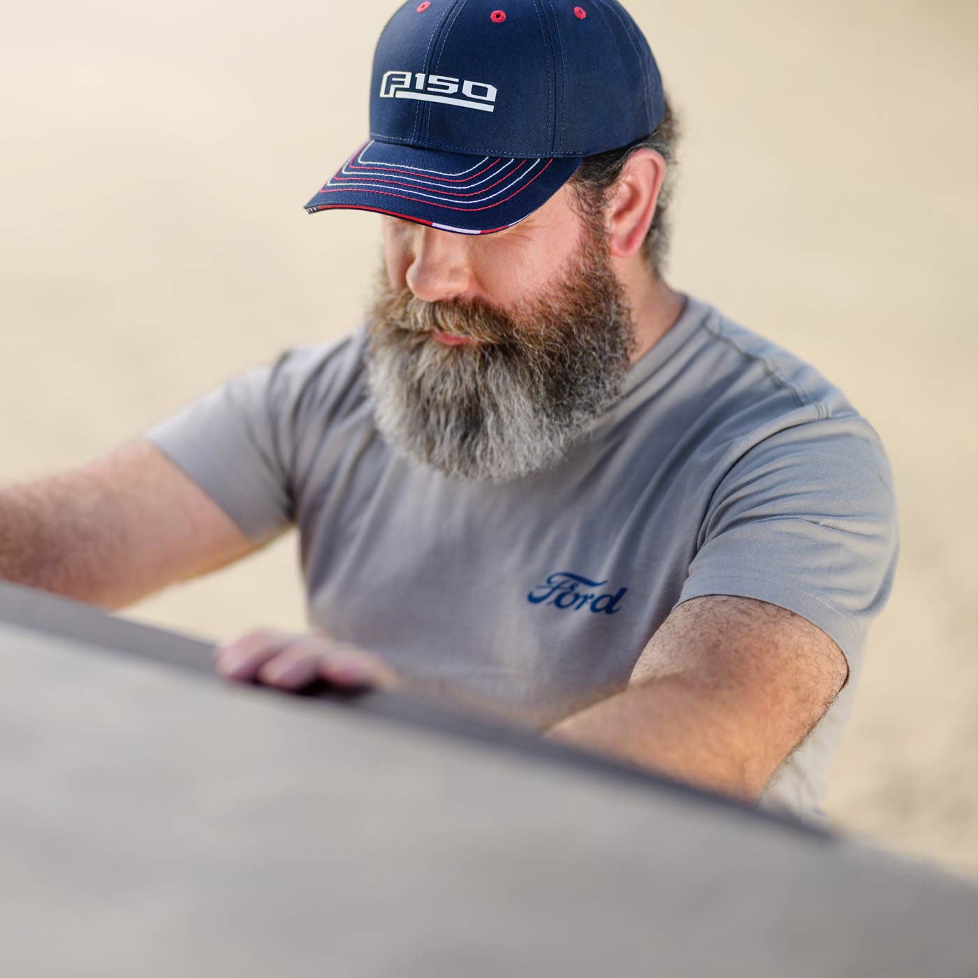 Man wearing a Ford cap and shirt, looking at a car.