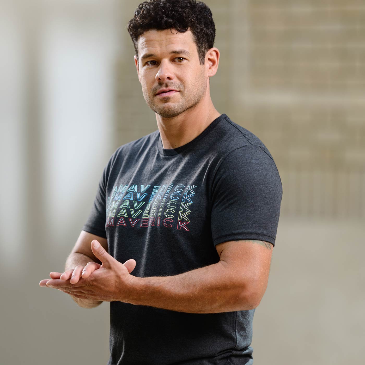 Man wearing a dark gray t-shirt with colorful text, standing against a neutral background