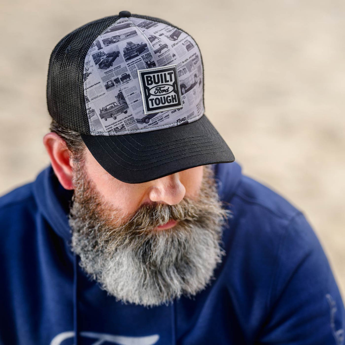 Man wearing a cap with vintage ford 'Built Ford Tough' logo and design, looking down.
