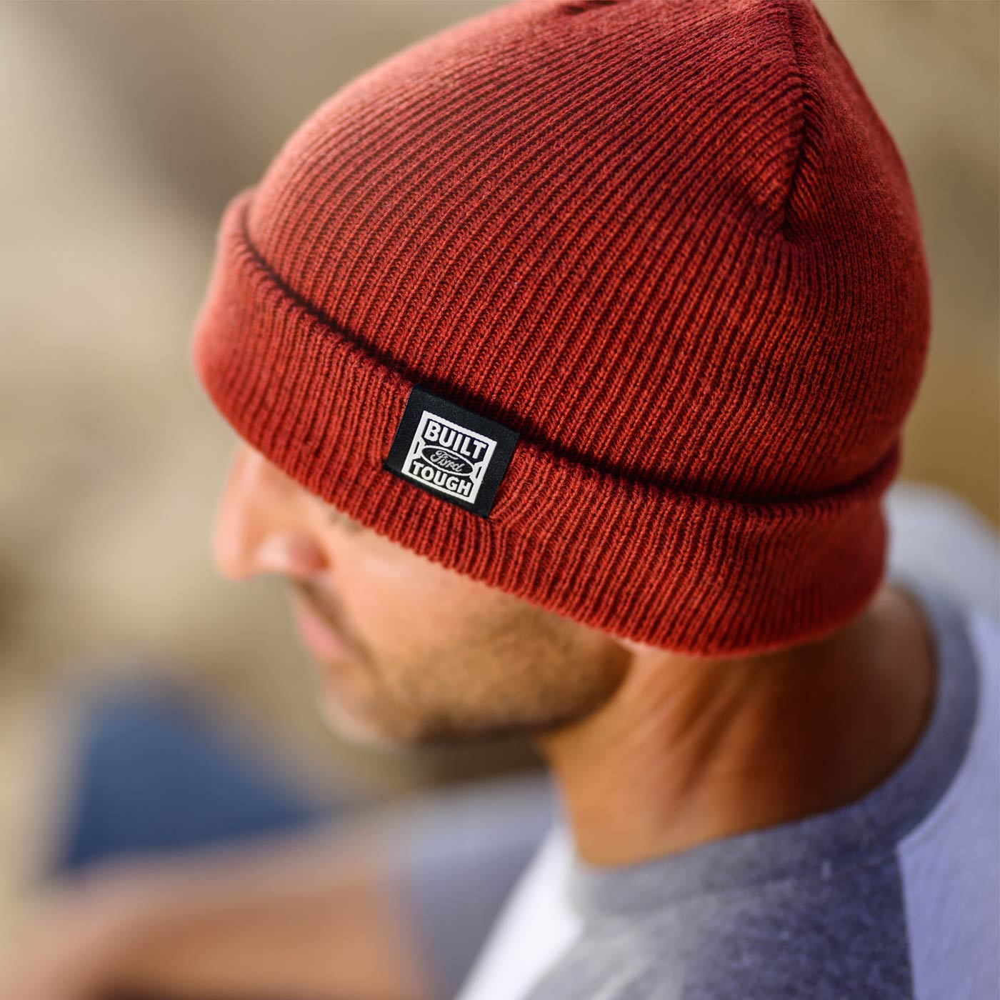 Red beanie with a brand logo worn by a person, blurred background