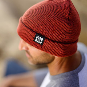 Red beanie with a brand logo worn by a person, blurred background