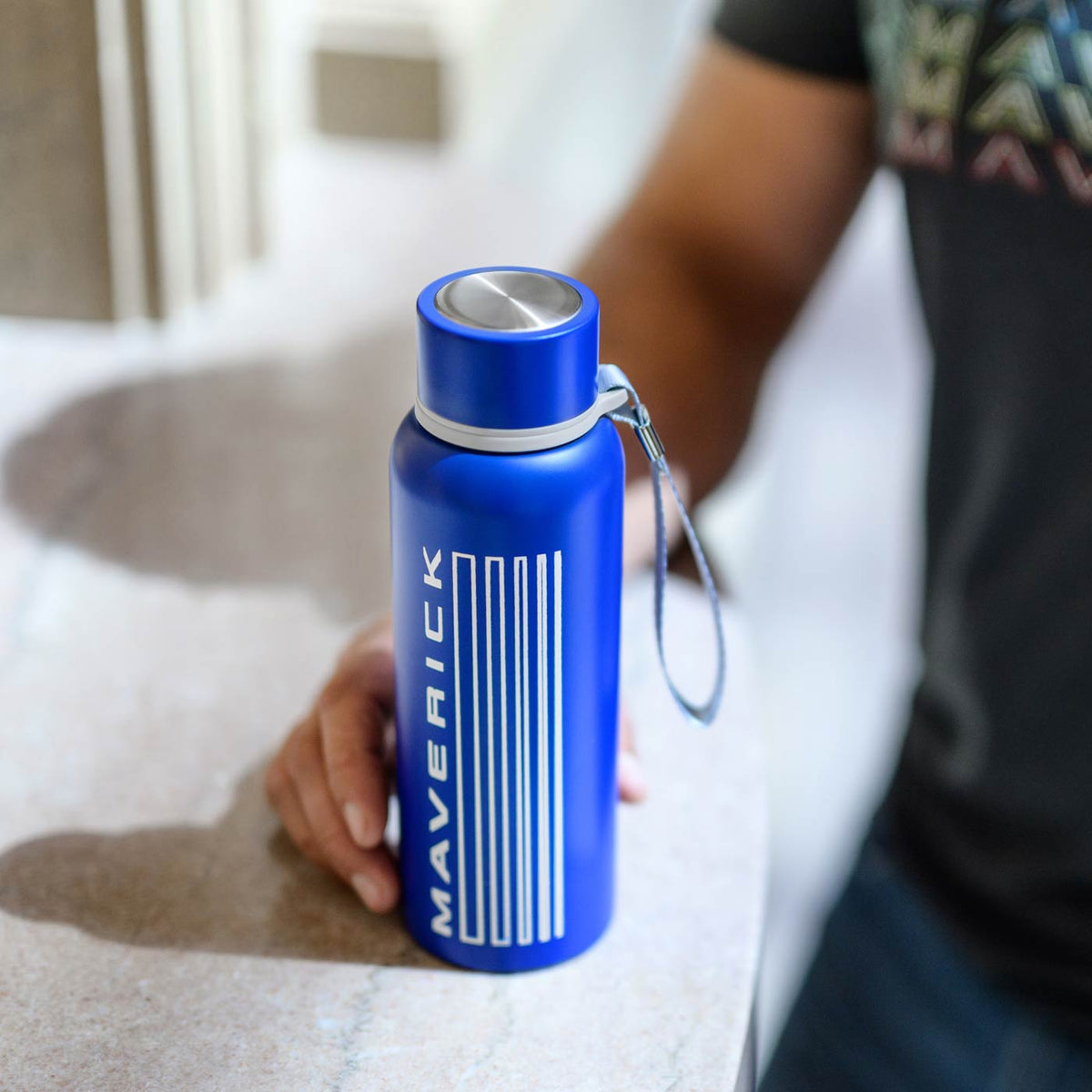 Blue water bottle with 'Maverick' branding held by a person on a bed.