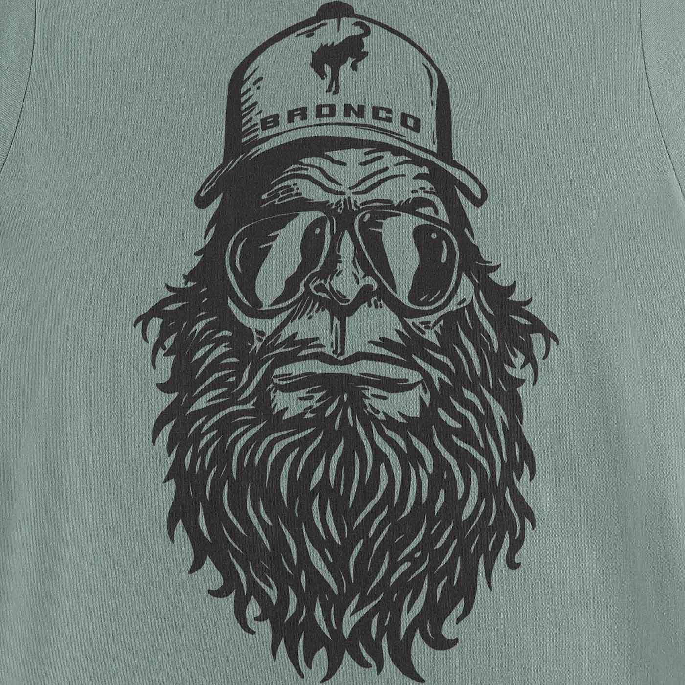 T-shirt with a graphic of a bearded man wearing goggles and a 'Bronco' cap on a green background