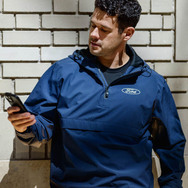 Man wearing a blue jacket with a Ford logo, standing against a brick wall.