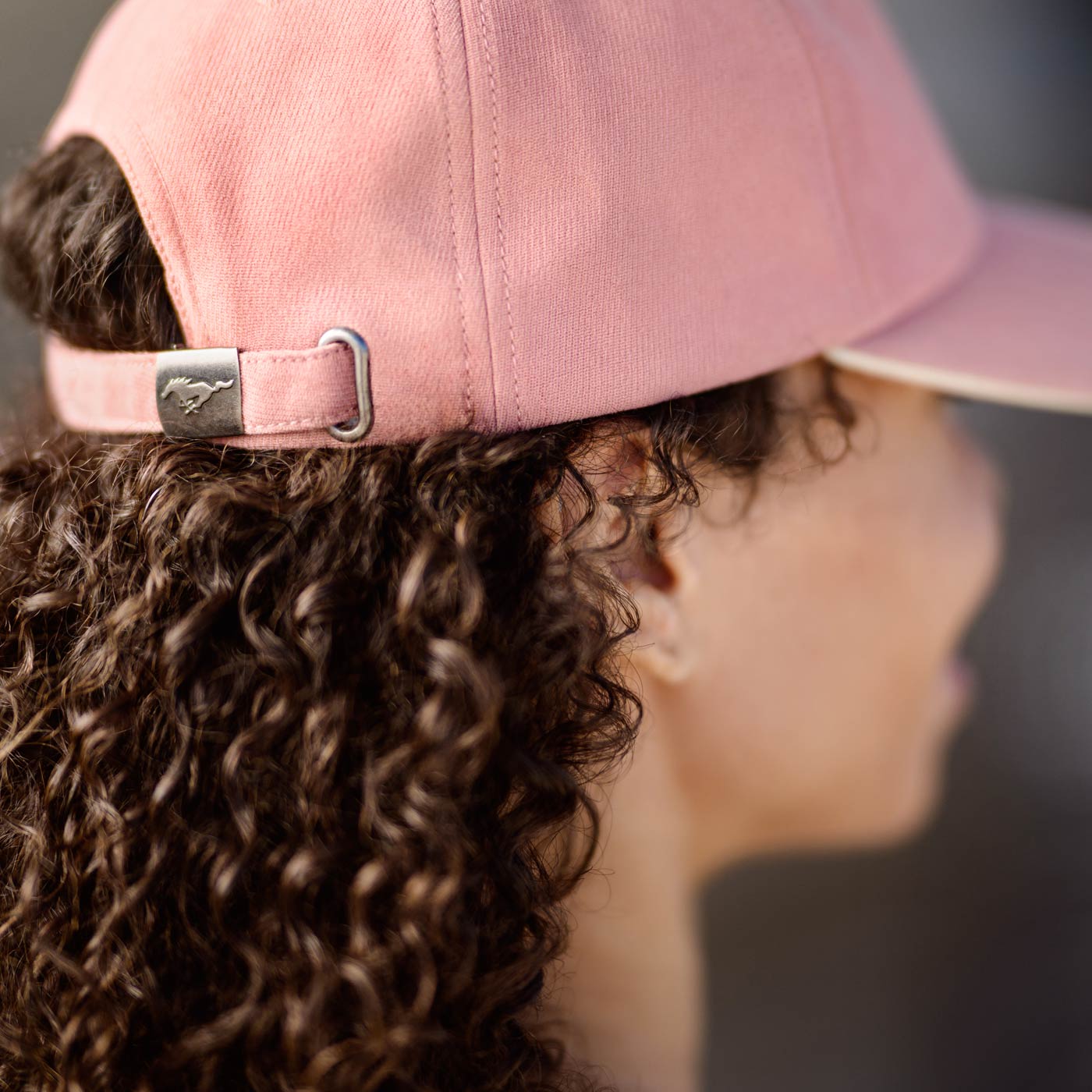 Person wearing a pink cap with a mustang logo, focusing on the cap and hair.