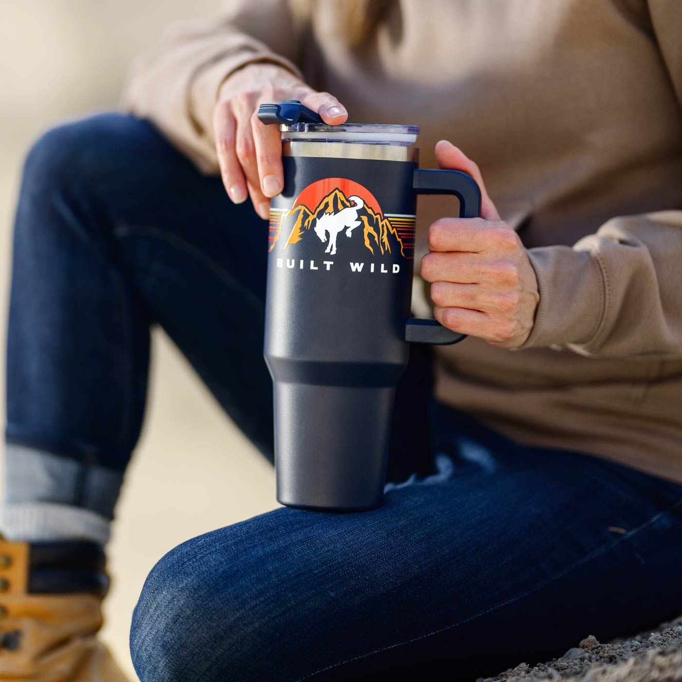 Person holding a black travel mug with 'Built Wild' logo