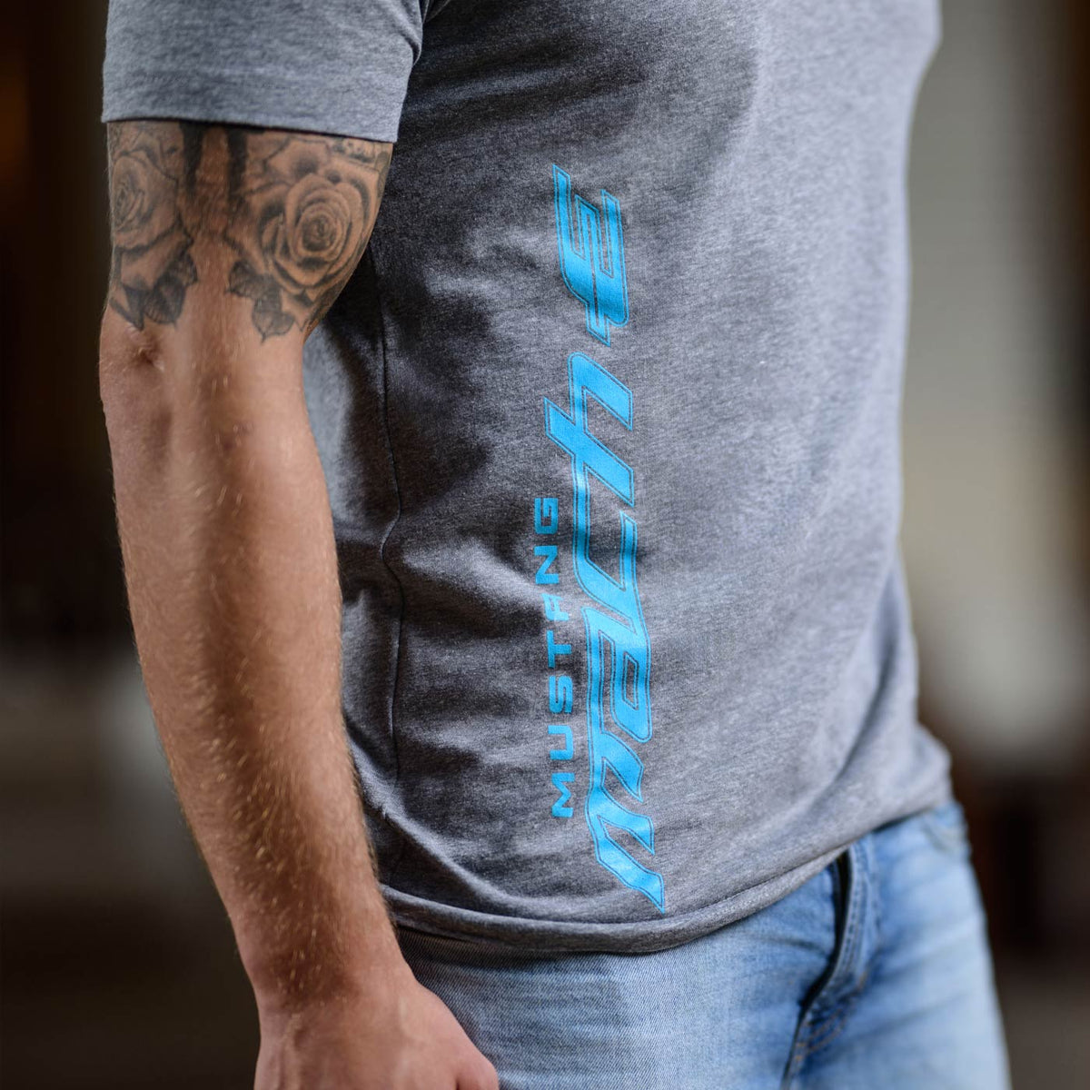 Person wearing a gray t-shirt with blue text and jeans, blurred background