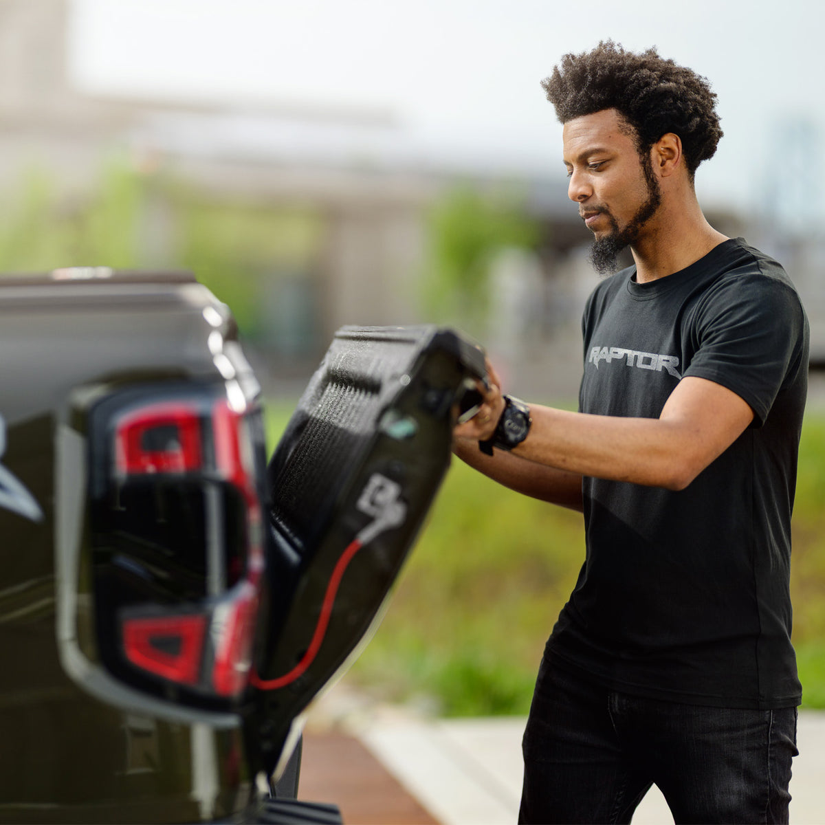 Man attaching a device to the back of a raptor vehicle with a blurred outdoor background