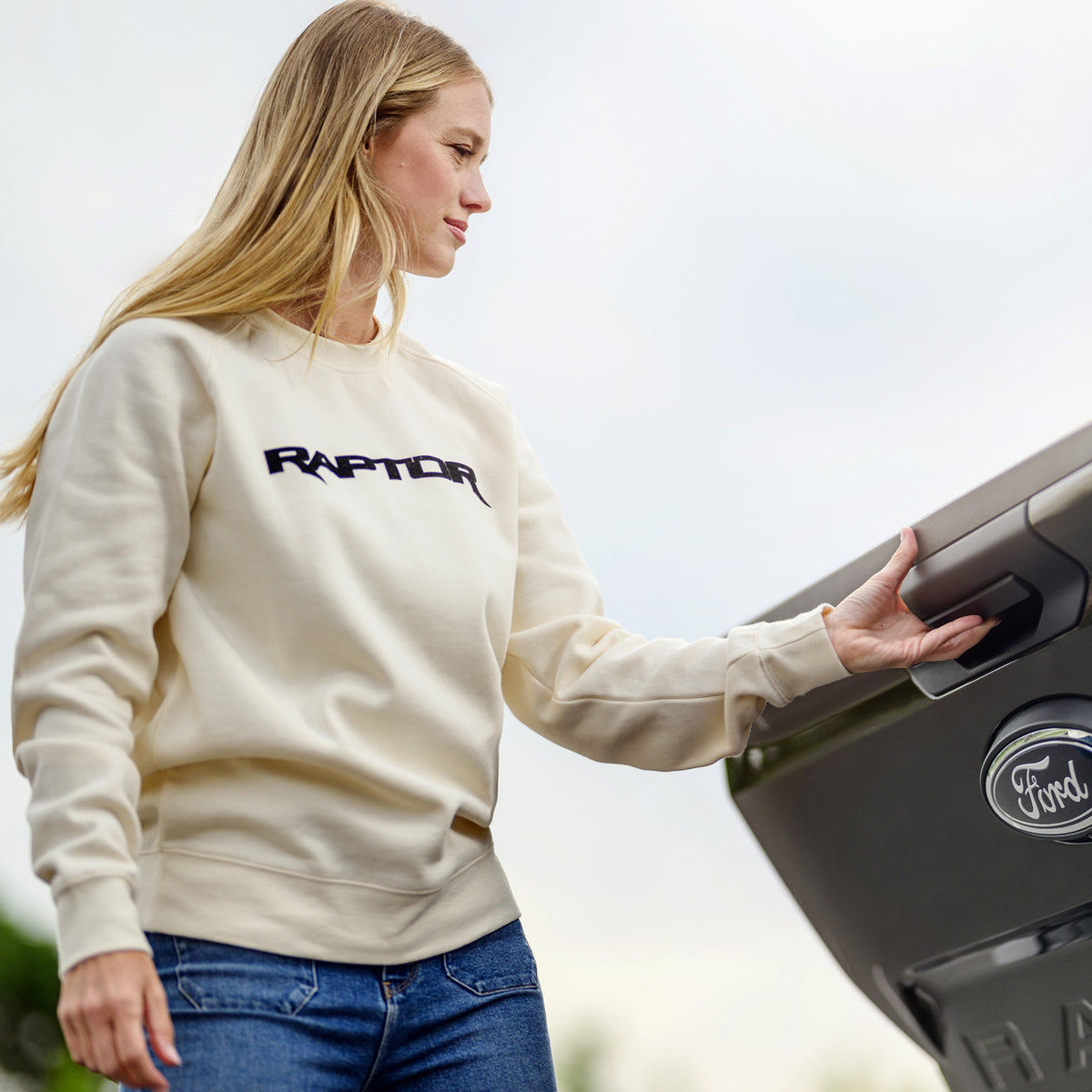 Person wearing a cream sweatshirt with 'Raptor' text, opening a Ford vehicle door.