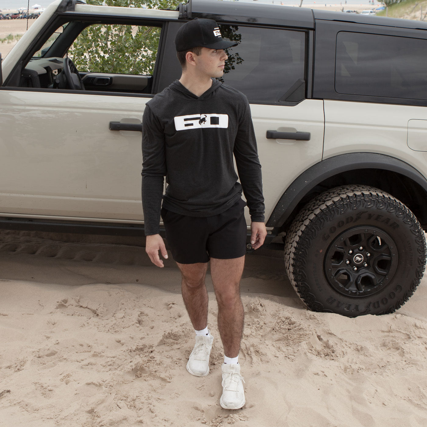Man standing in front of a beige SUV on sandy terrain