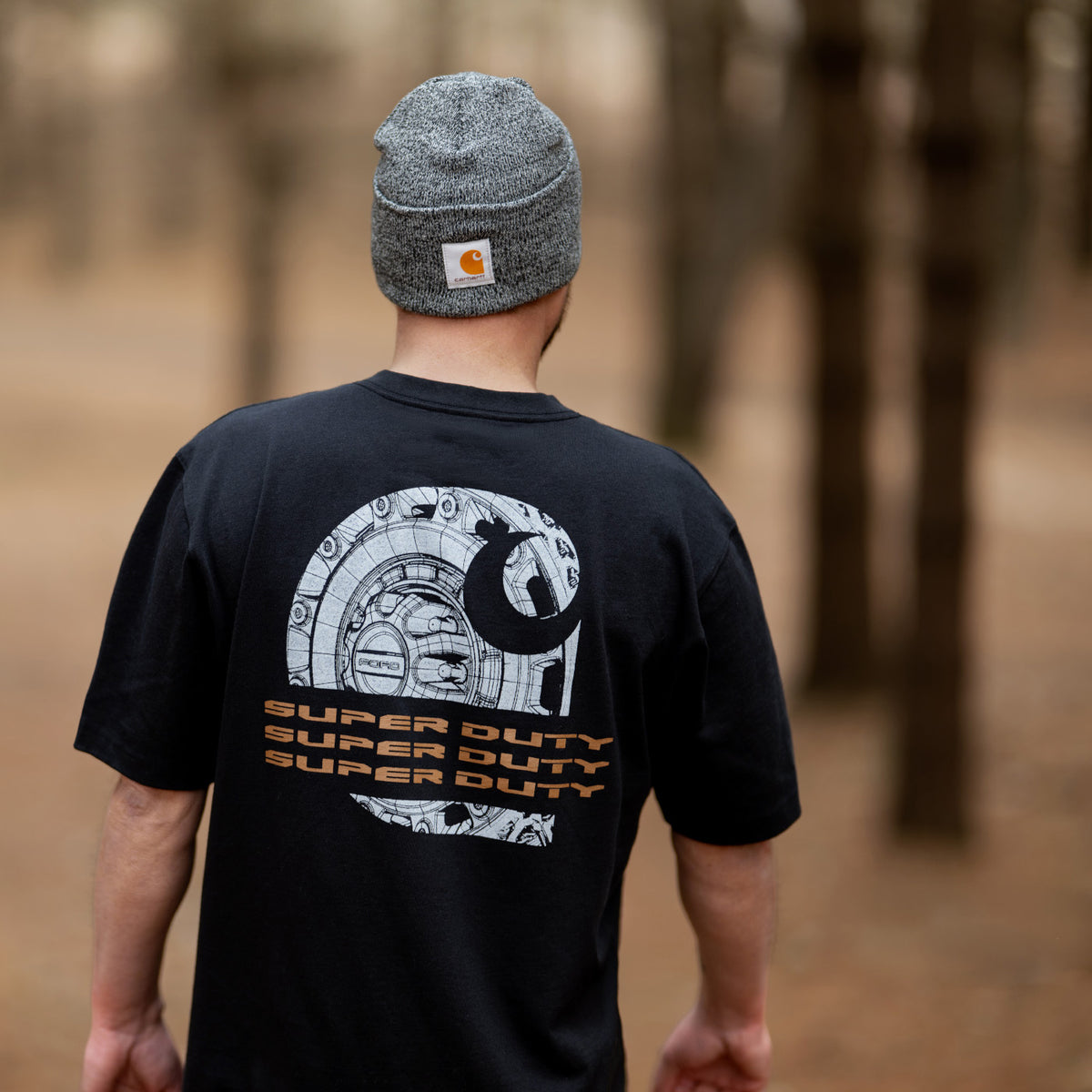 Person wearing a black t-shirt with a graphic design and 'Super Duty' text, standing in a forest.