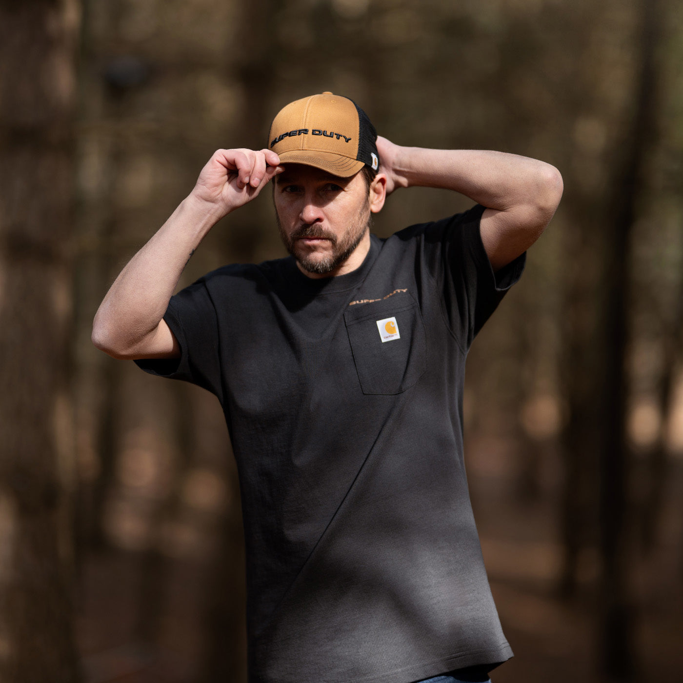 Man wearing a black t-shirt and brown cap with 'Carhartt' branding in a forest setting.