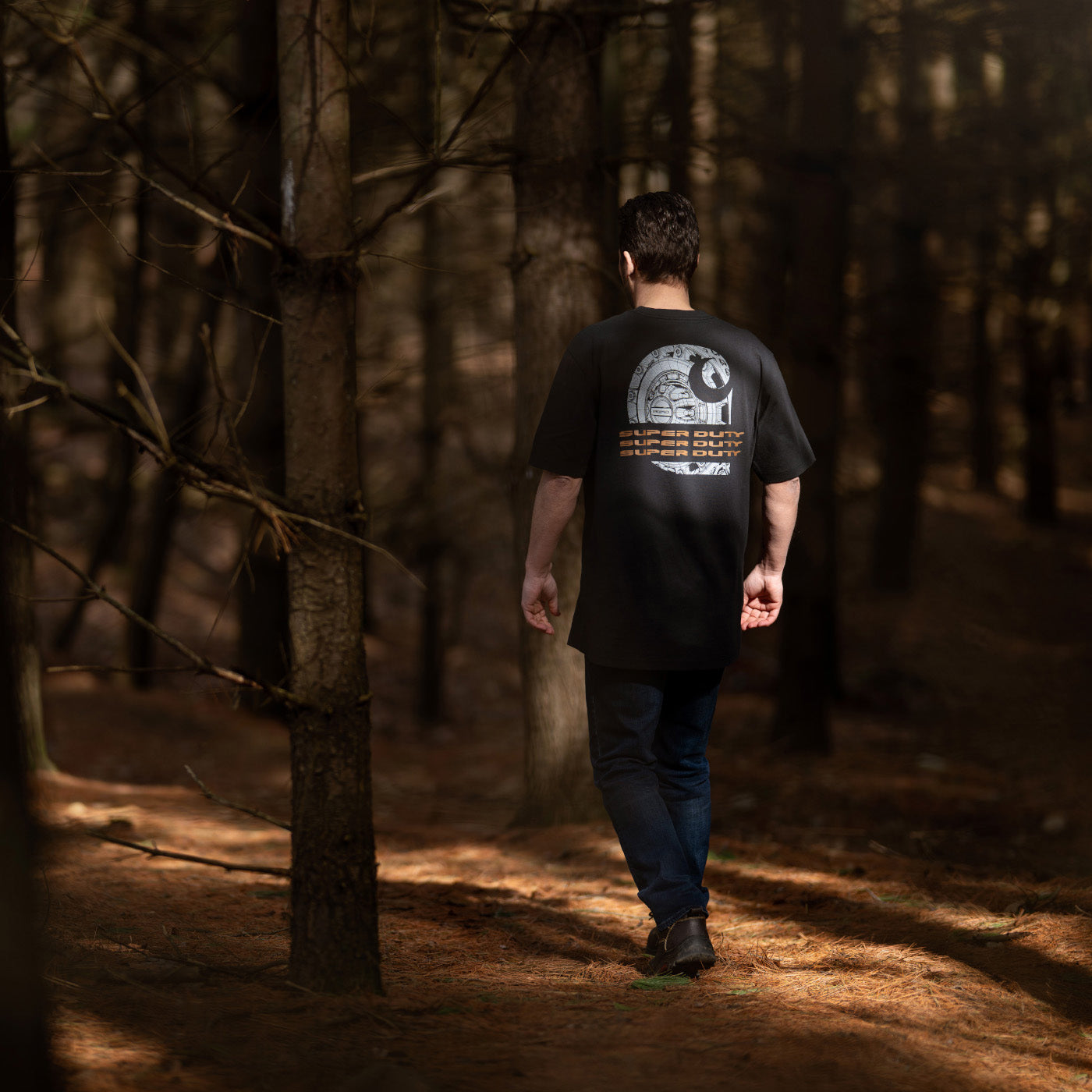 Man walking through a forest wearing a black t-shirt with a graphic ford super duty design on the back.