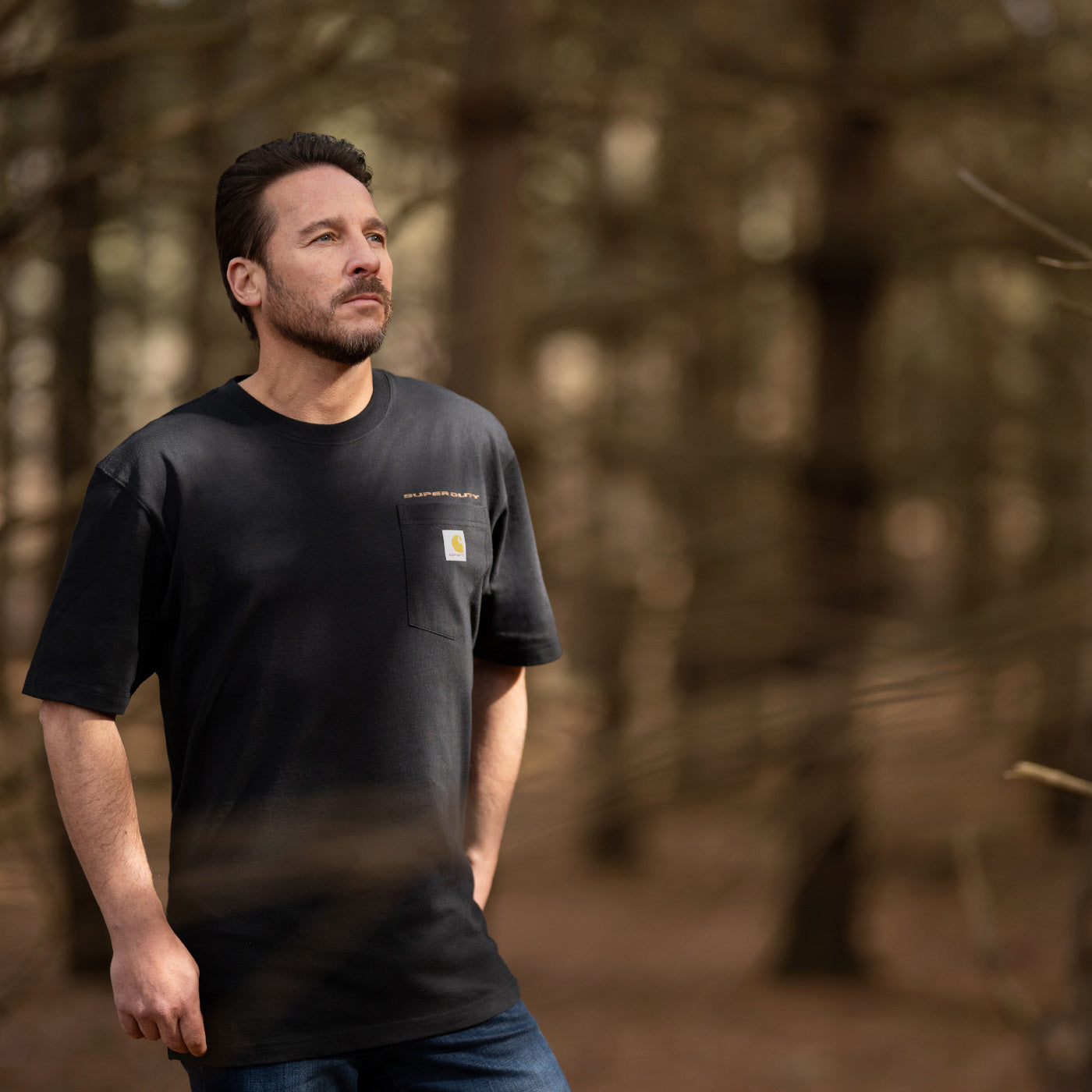 Man wearing a black t-shirt with a carhartt and super duty logo in a forest setting