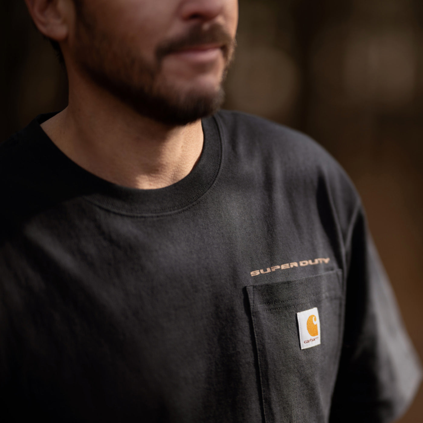 Person wearing a black Carhartt shirt with a logo on a blurred background