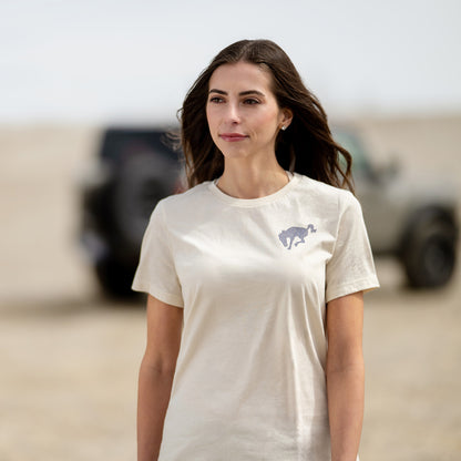 Woman wearing a white t-shirt with a logo in a desert-like setting