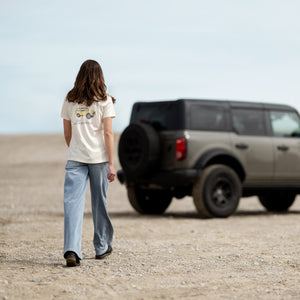 Person walking towards a parked SUV in a desert-like setting