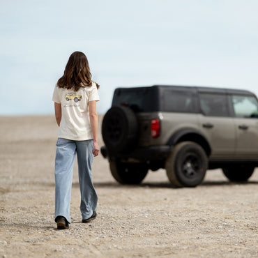 Person walking towards a parked SUV in a desert-like setting