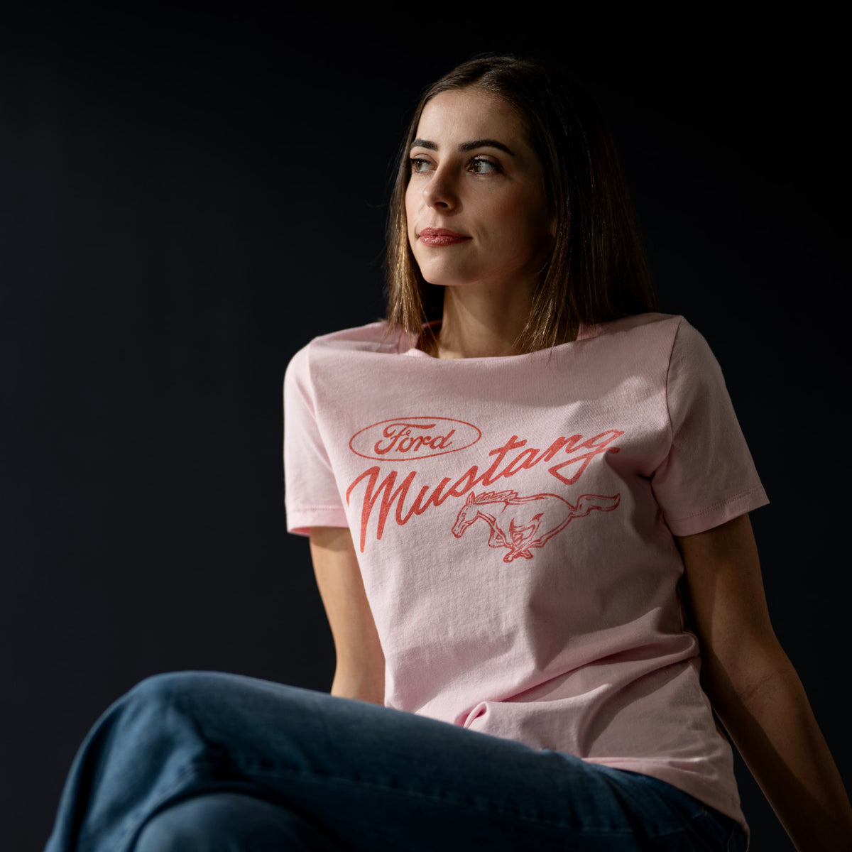 Woman wearing a pink t-shirt with 'Ford Mustang' logo against a dark background