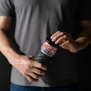 Person holding a black insulated mug with colorful labels against a dark background
