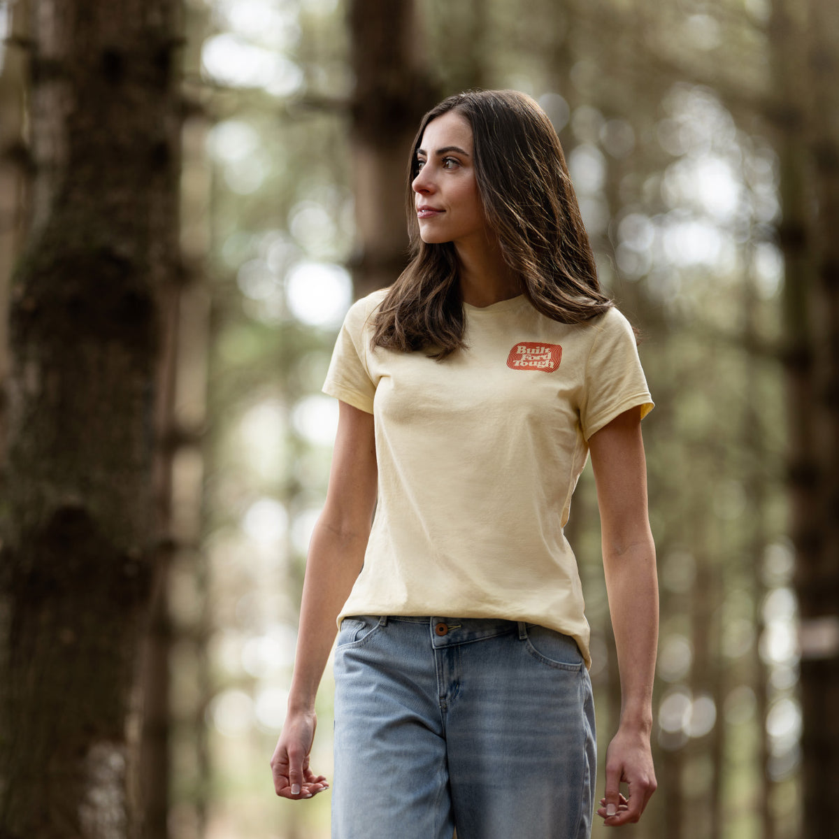 Woman wearing a beige t-shirt with a logo in a forest setting