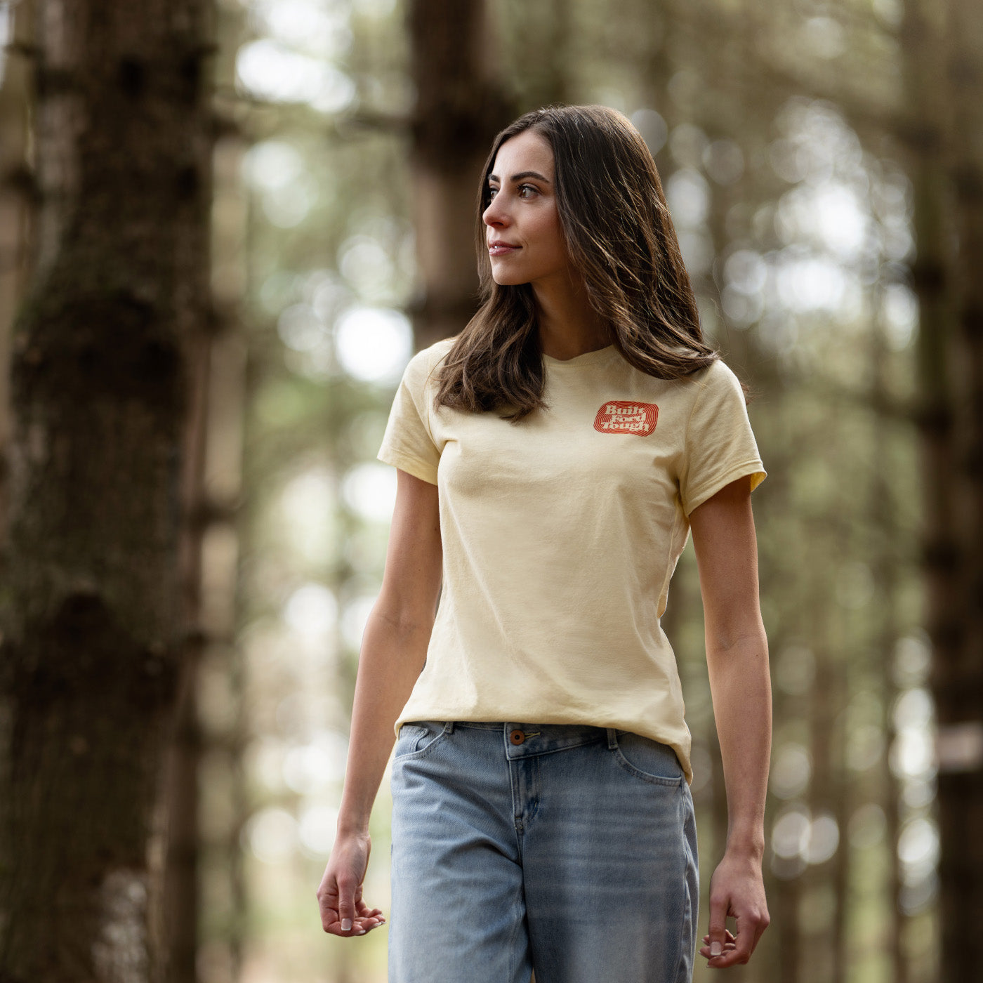 Woman wearing a beige t-shirt with a logo in a forest setting