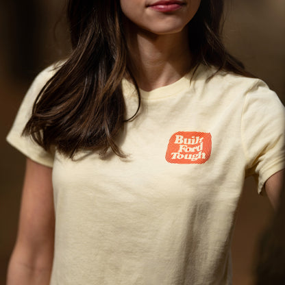 Person wearing a beige t-shirt with a red and white logo on a blurred background