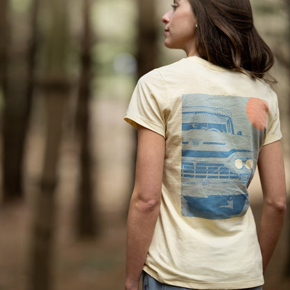 Person wearing a beige t-shirt with a graphic design on the back, standing in a forest.