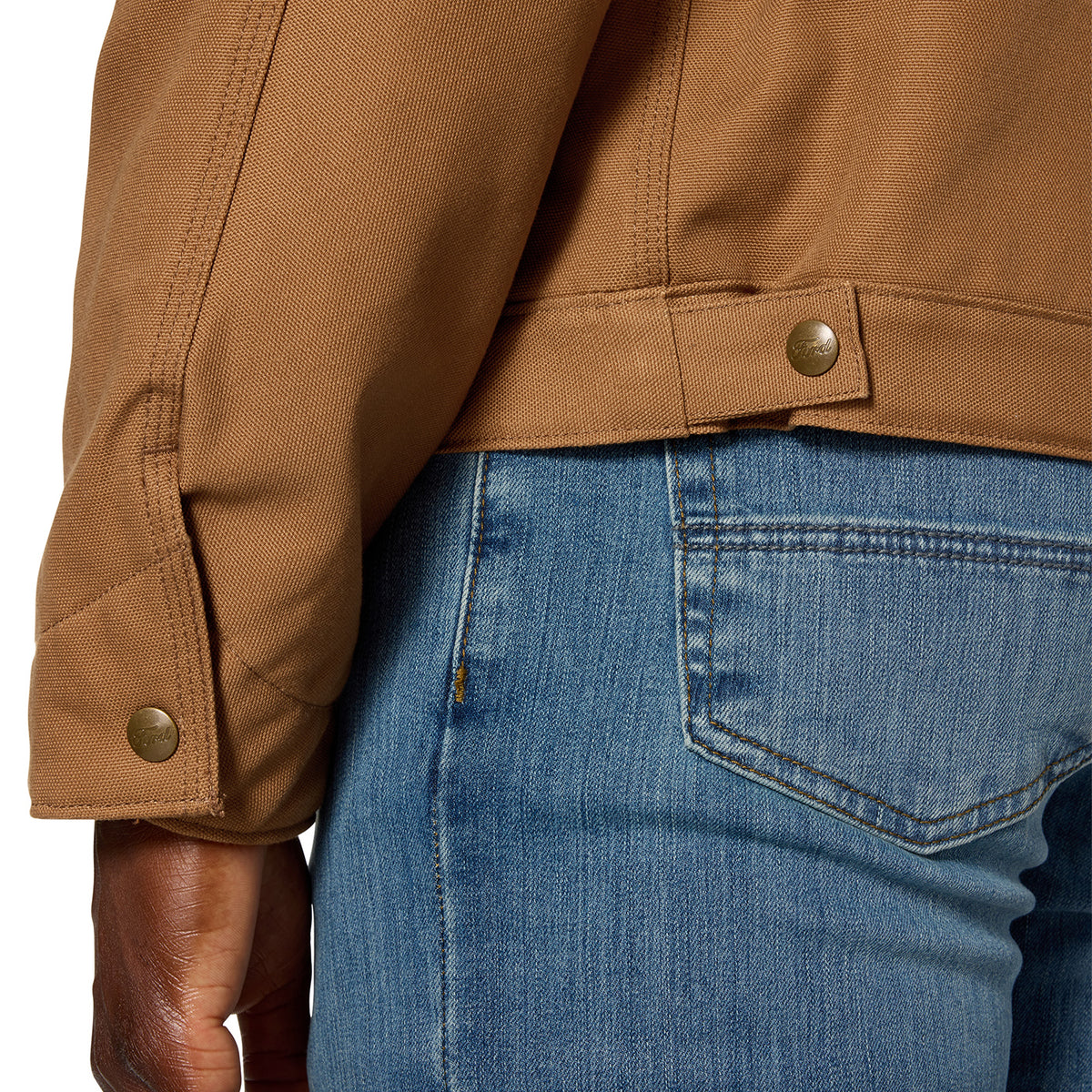 Close-up of a person wearing a tan work jacket with a buttoned cuff and a brown leather belt, paired with blue jeans.