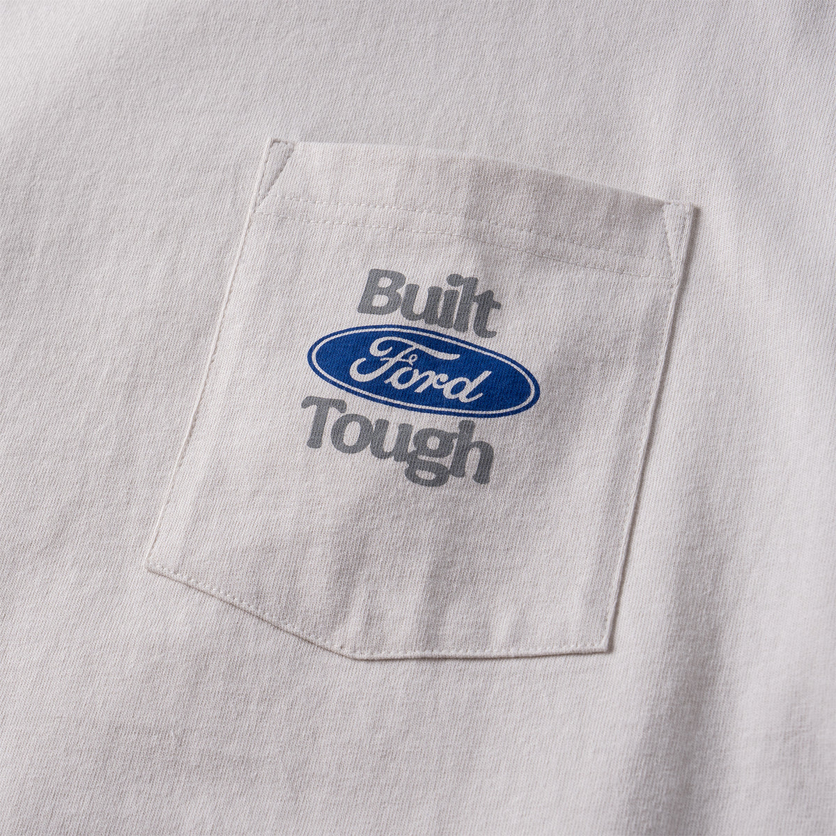 Close-up of a white pocket tee featuring a chest pocket with 'Built Ford Tough' embroidered in gray and the blue oval Ford logo.