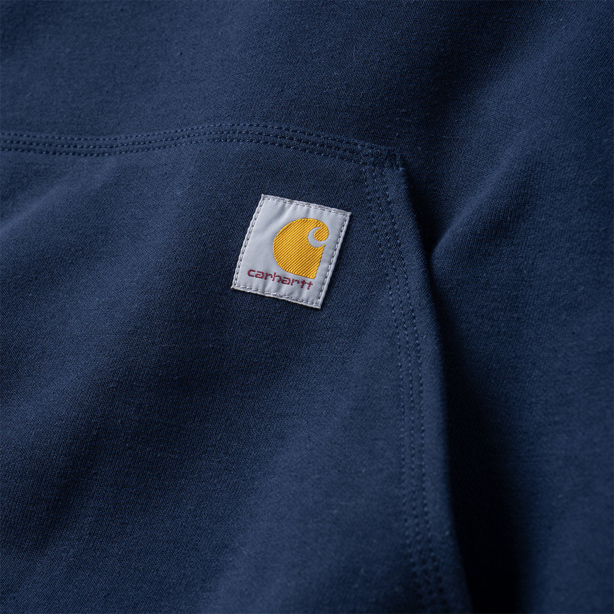 Close-up of a navy blue knit garment with a small white Carhartt brand patch featuring a yellow logo on the chest.