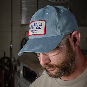 A man wearing a light blue denim baseball cap with a 'Fred Motor Co. Detroit, Mich.