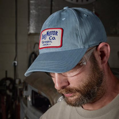 A man wearing a light blue denim baseball cap with a 'Fred Motor Co. Detroit, Mich.