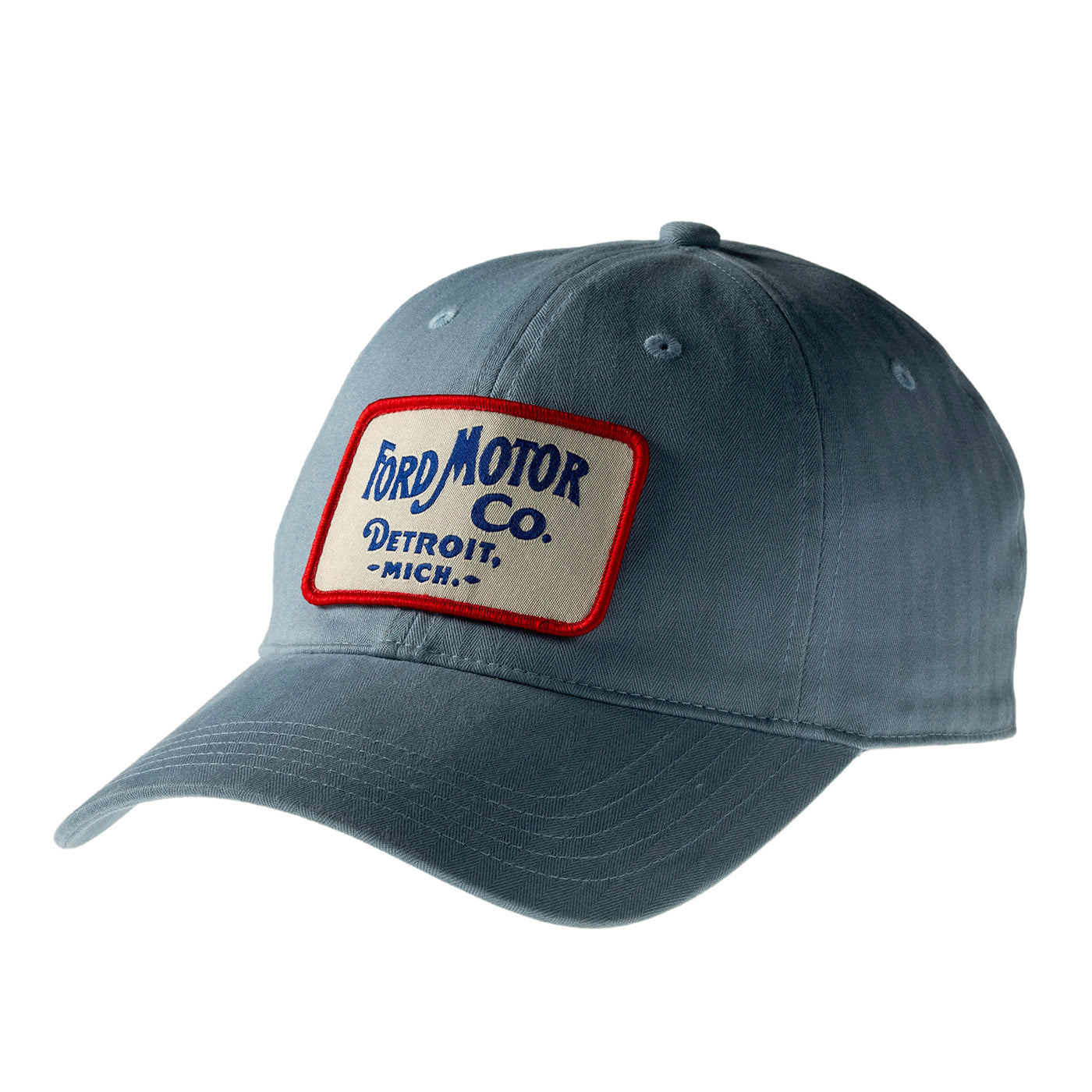 A slate blue baseball cap featuring a rectangular embroidered patch on the front with 'Ford Motor Co. Detroit, Mich.
