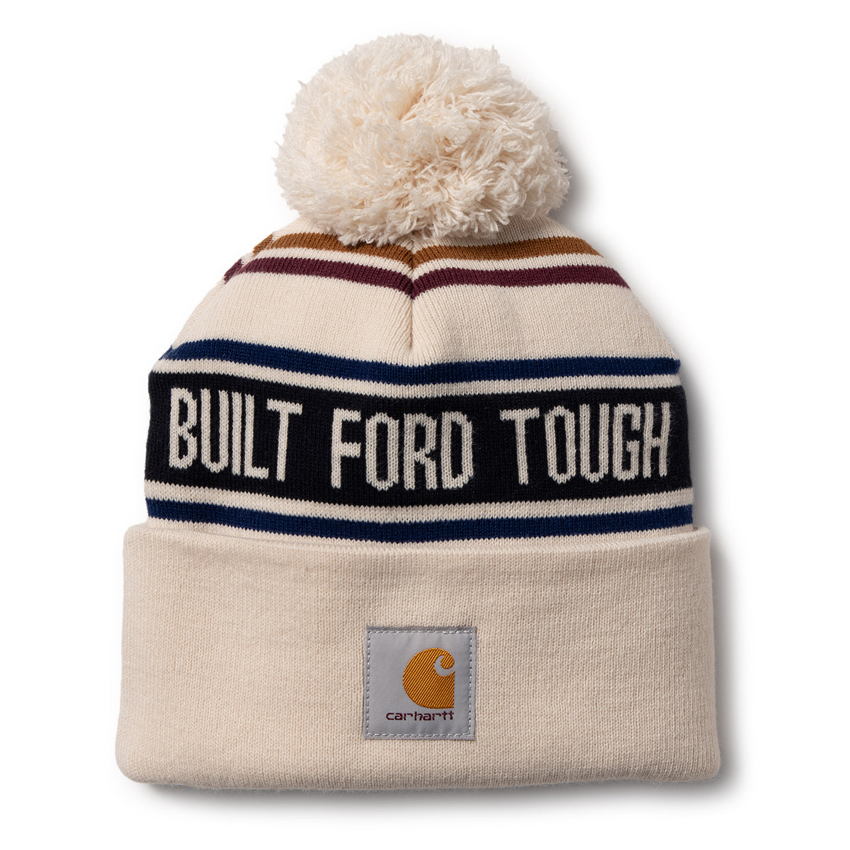 A cream-colored knit pom-pom beanie hat featuring navy, burgundy, and gold stripes, a black band with white text reading 'BUILT FORD TOUGH', and a gray Carhartt logo patch on the cuff.