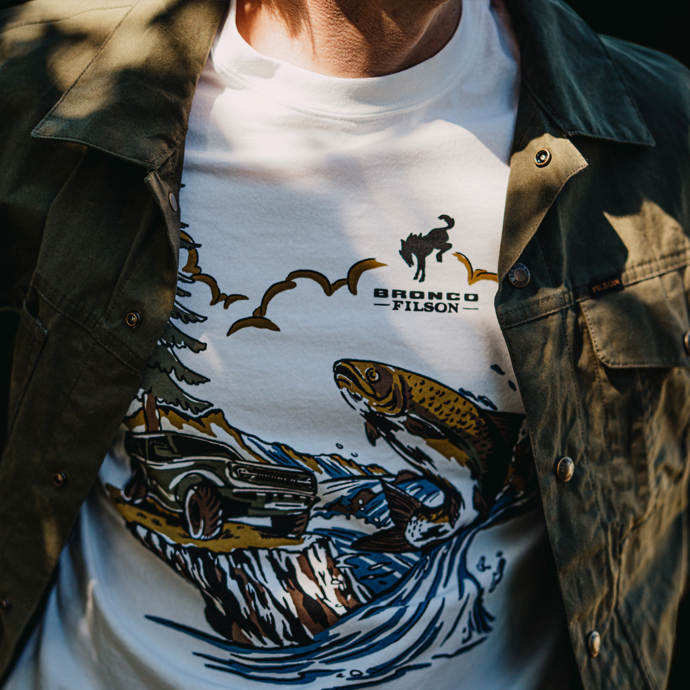 Person wearing a white t-shirt with a graphic design and 'Bronco Filson' branding.