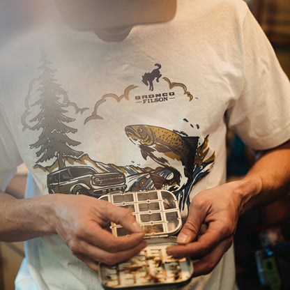 Person wearing a white t-shirt with a graphic design, holding a small container.