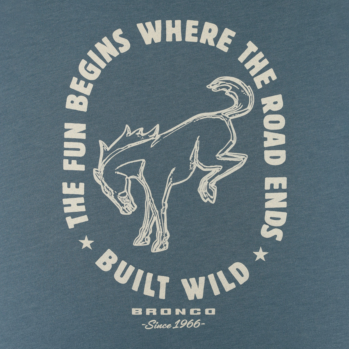 A close-up of a blue-gray heathered t-shirt featuring a vintage-style graphic print. The design displays a white line-art illustration of a bronco surrounded by the text 'THE FUN BEGINS WHERE THE ROAD ENDS' and 'BUILT WILD', with 'BRONCO Since 1966' printed below.