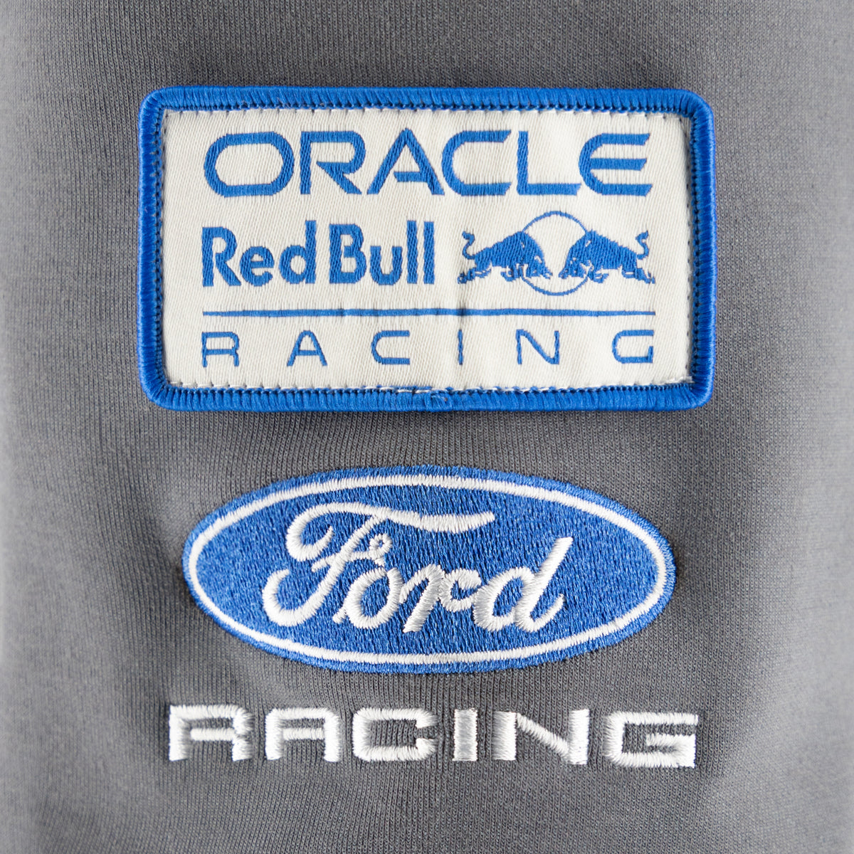 Close-up of embroidered racing team patches on a gray fabric background, including an Oracle Red Bull Racing patch and a Ford Racing patch.