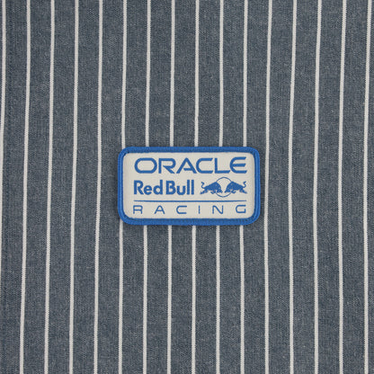 A rectangular embroidered patch with a white background and blue border, featuring the text 'ORACLE Red Bull RACING' and the Red Bull logo, placed on a blue and white vertically striped fabric background.